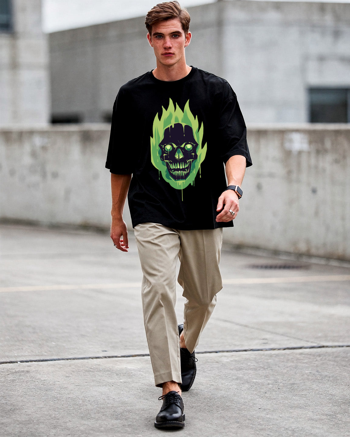 Man wearing a black t-shirt with a colorful skull design, beige pants, and black shoes on a concrete surface.