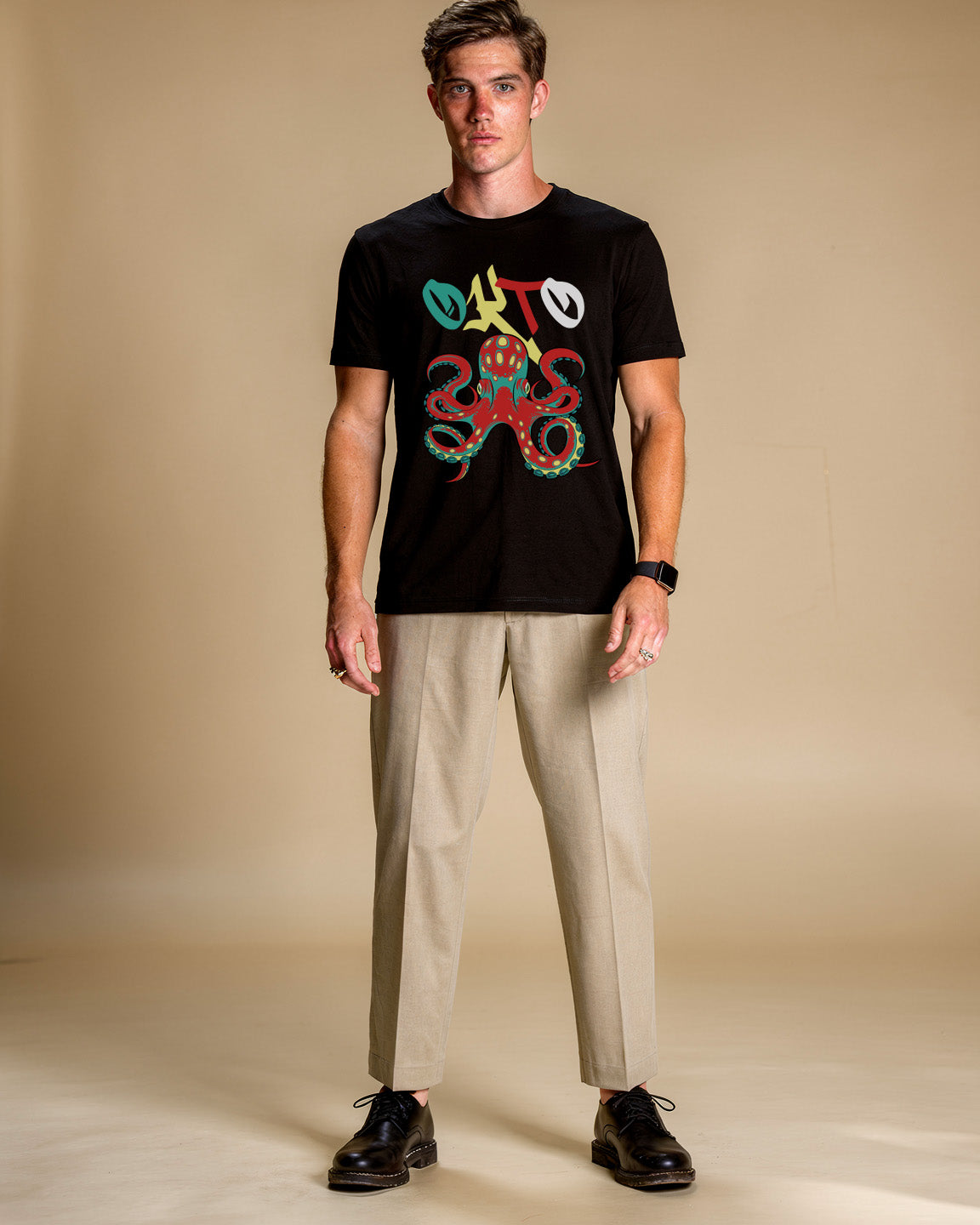 Man wearing a black t-shirt with colorful graphic design and beige pants on a beige background