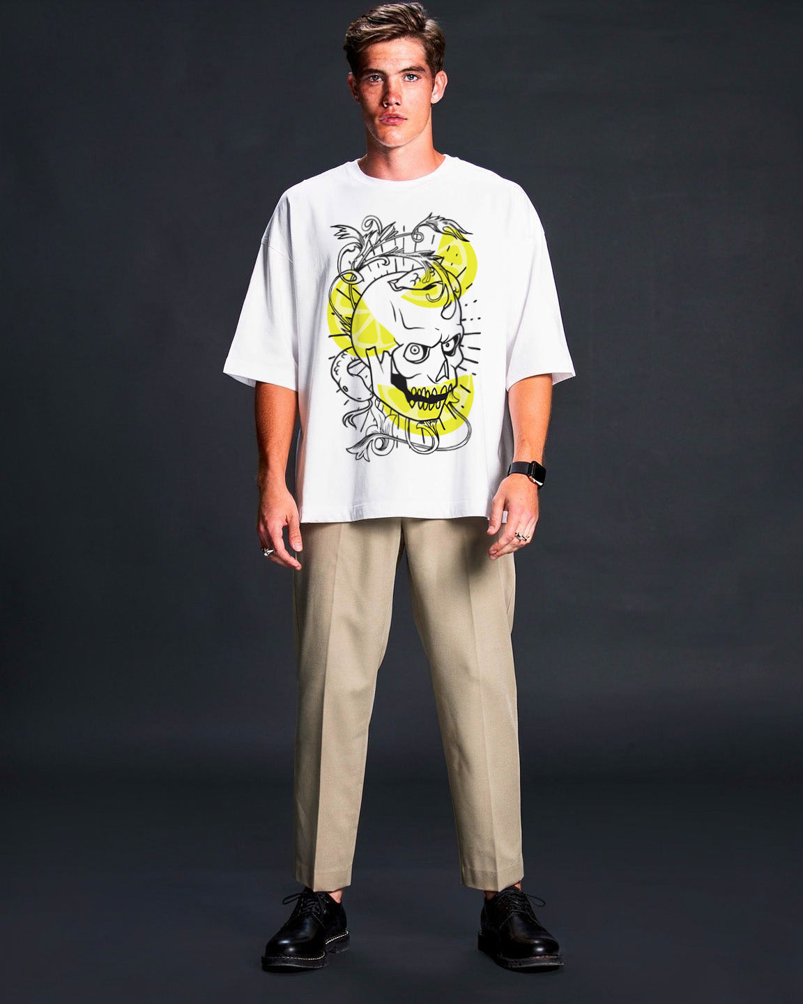 Man wearing a white t-shirt with a graphic design and beige pants on a dark background