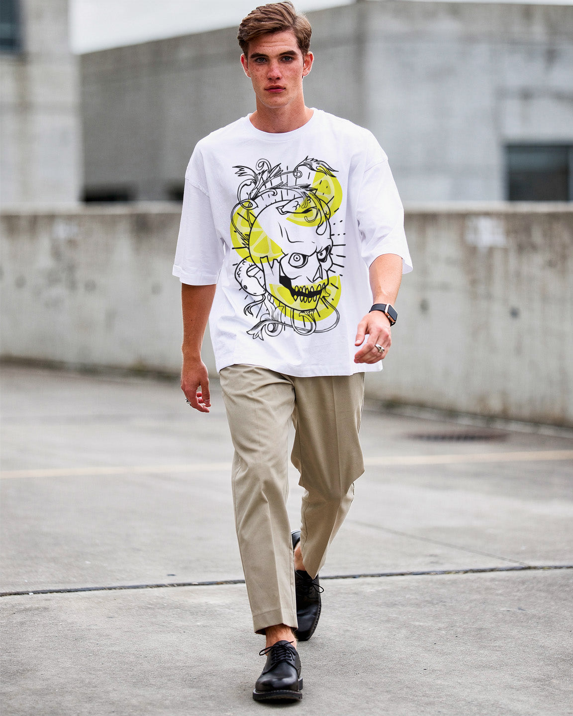 Man wearing a white t-shirt with a graphic design, beige pants, and black shoes walking on a concrete surface.
