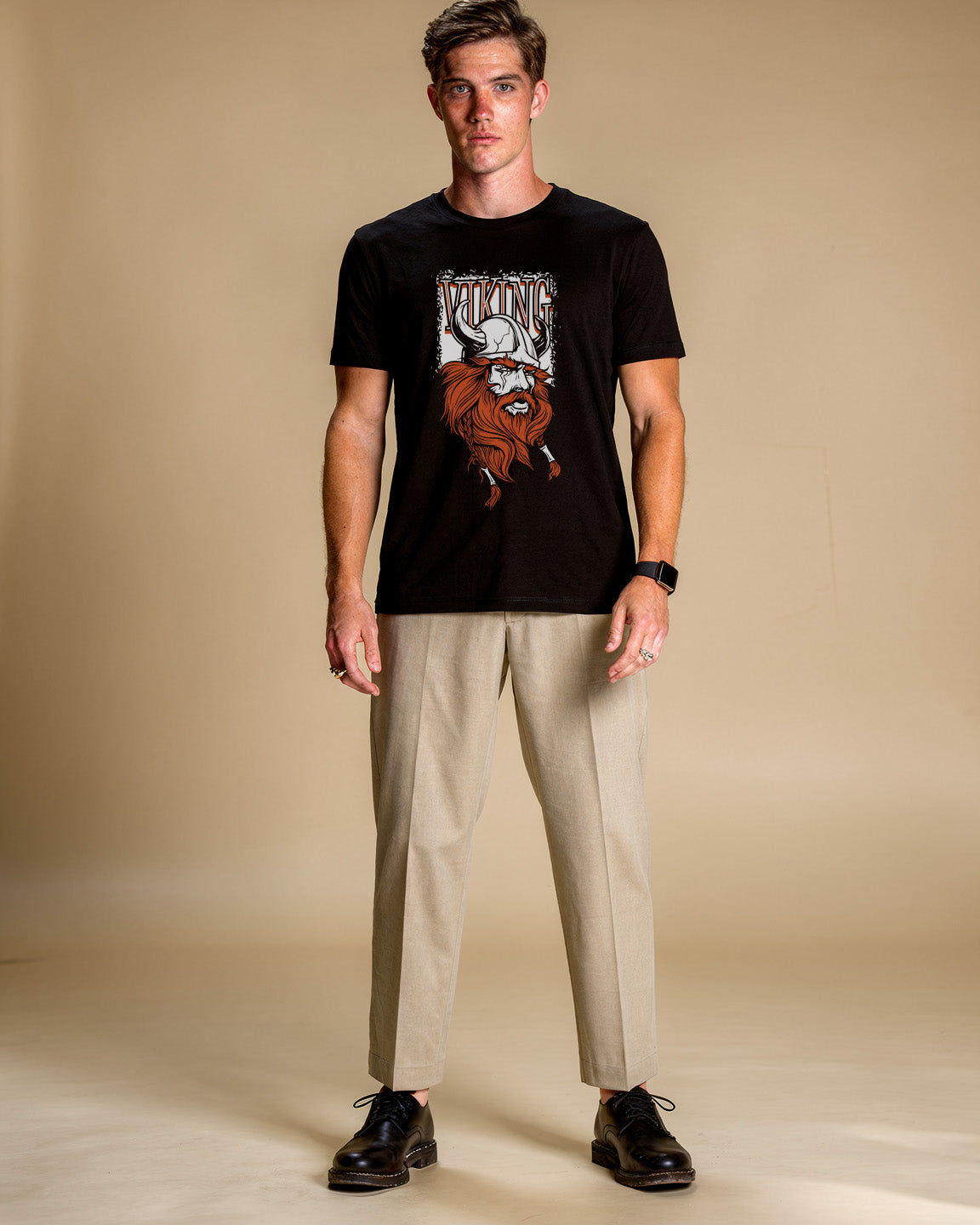 Man wearing a black t-shirt with a graphic design and beige pants on a beige background