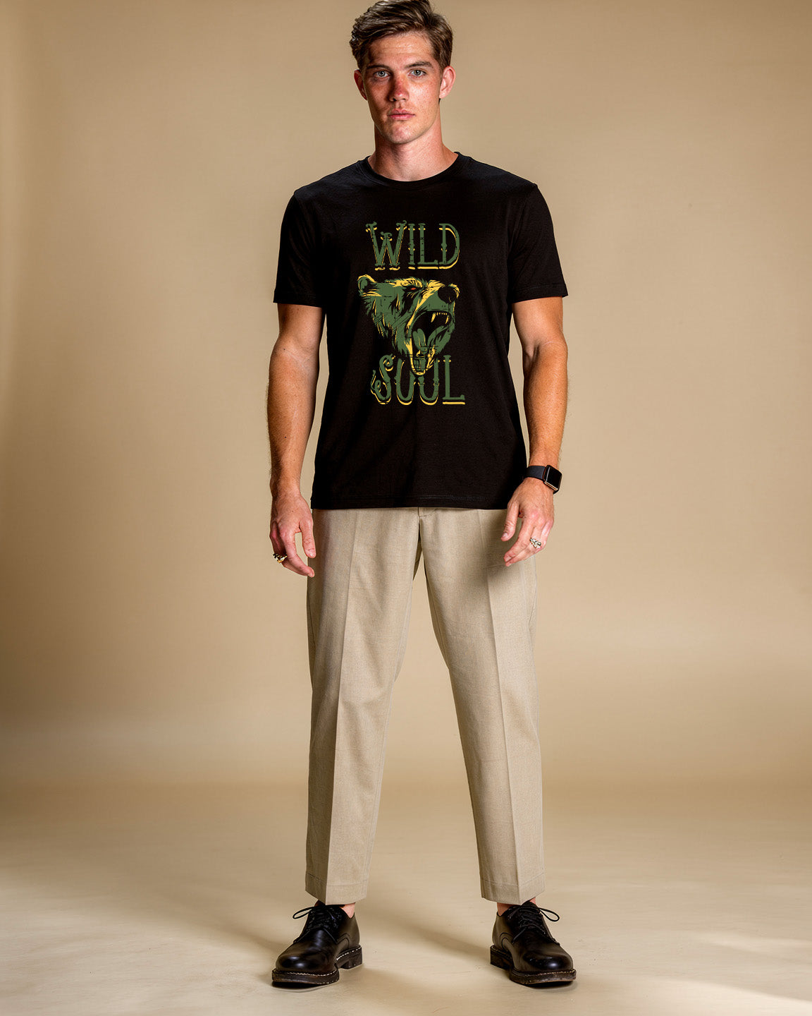 Man wearing a black t-shirt with 'Wild Soul' design and beige pants on a beige background