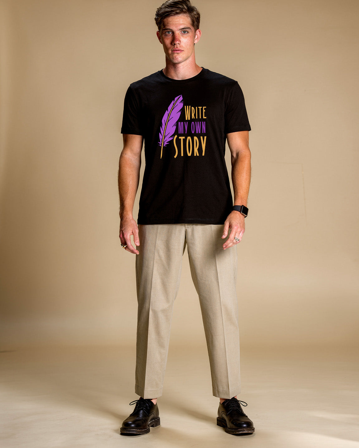 Man wearing a black t-shirt with 'Write My Own Story' text and a purple feather graphic on a beige background