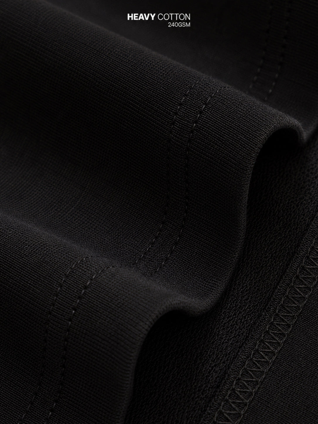 Close-up of black heavy cotton fabric with visible weave texture, stitched edges, and a small text overlay reading 'HEAVY COTTON 240GSM' at the top.