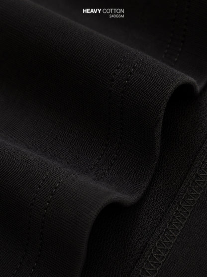 Close-up of black heavy cotton fabric with visible weave texture, stitched edges, and a small text overlay reading 'HEAVY COTTON 240GSM' at the top.