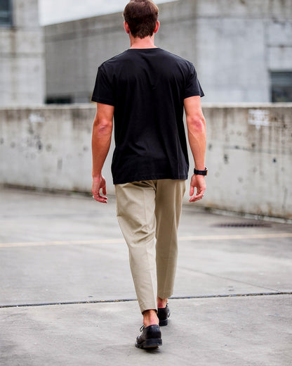 Man walking on a rooftop wearing a black t-shirt and beige pants.