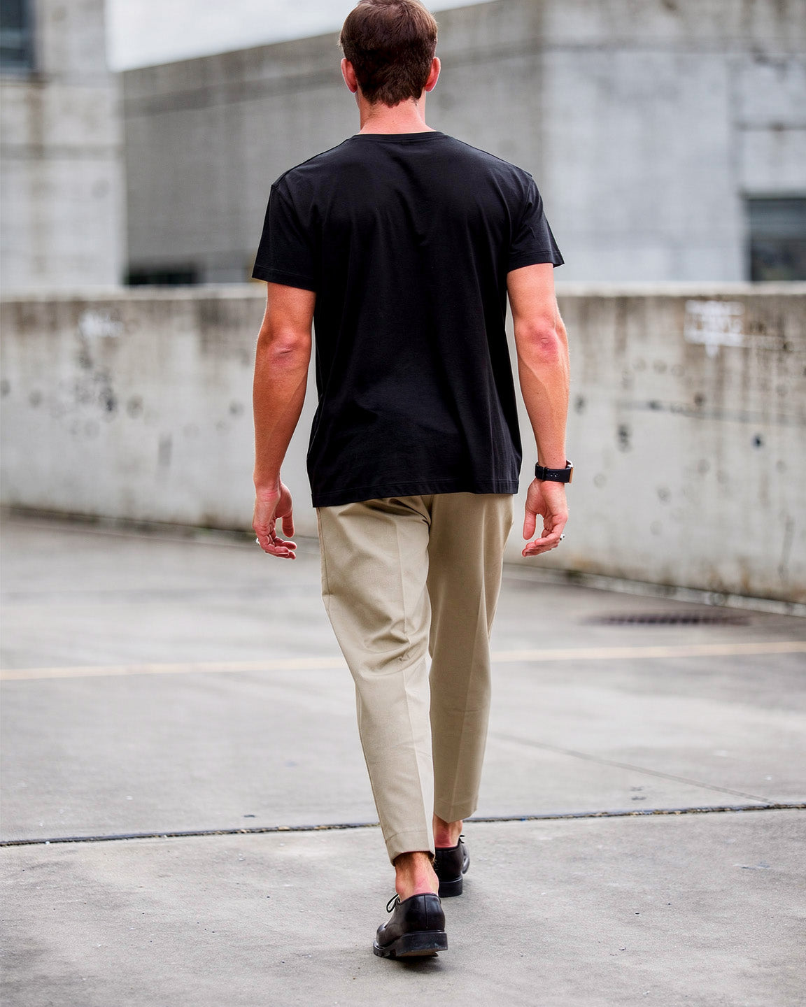 Man walking on a rooftop wearing a black t-shirt and beige pants.