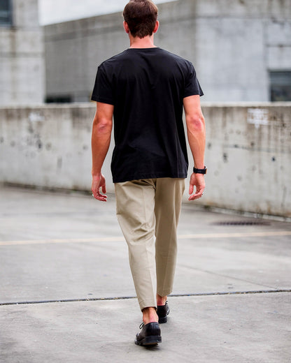 Man walking on a rooftop wearing a black t-shirt and beige pants.