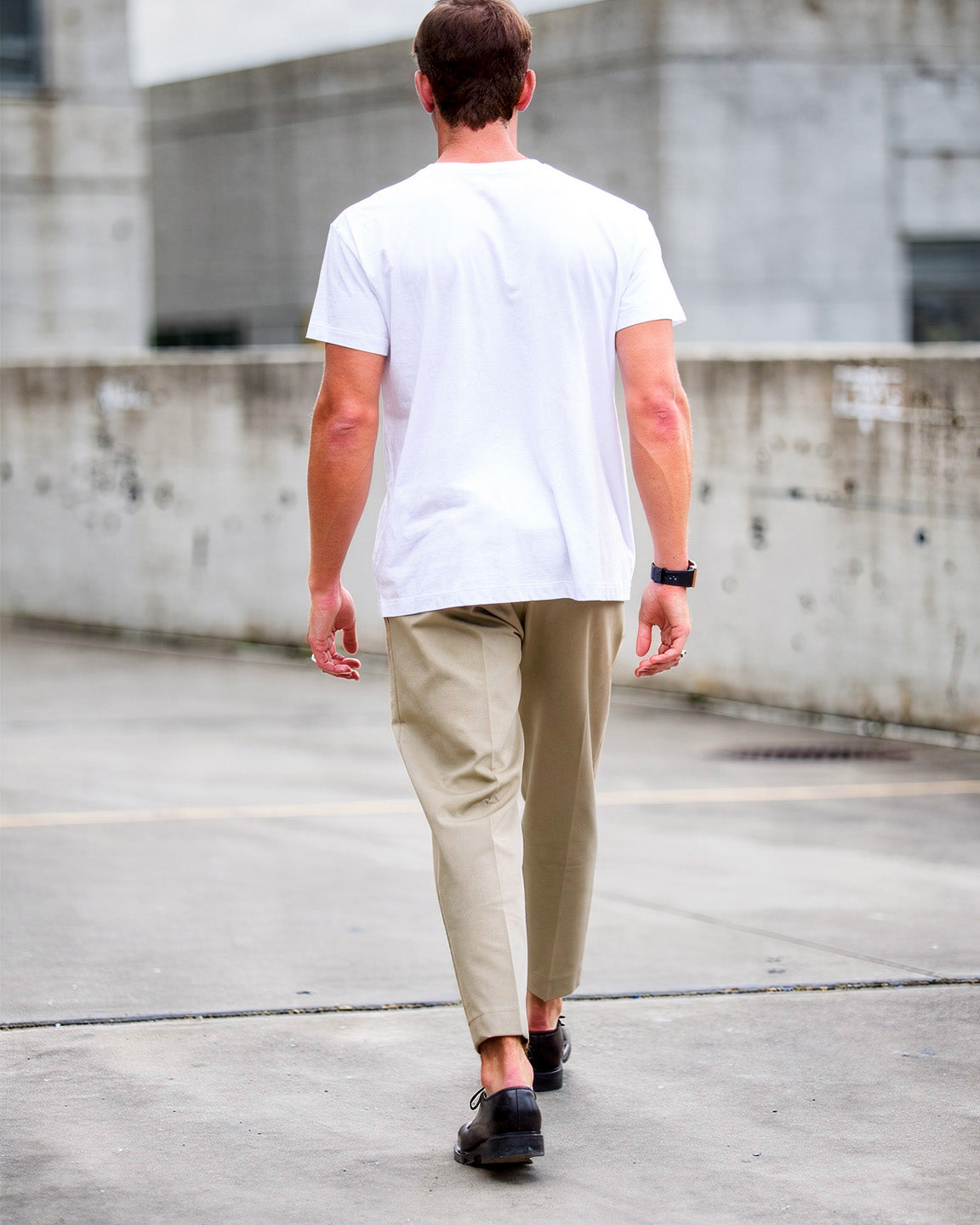 Man walking on a concrete surface wearing a white t-shirt and beige pants.