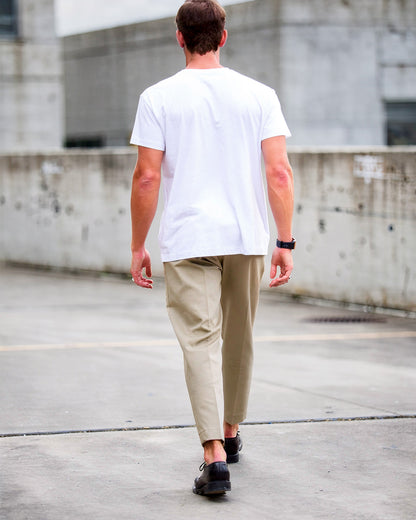 Man walking on a concrete surface wearing a white t-shirt and beige pants.