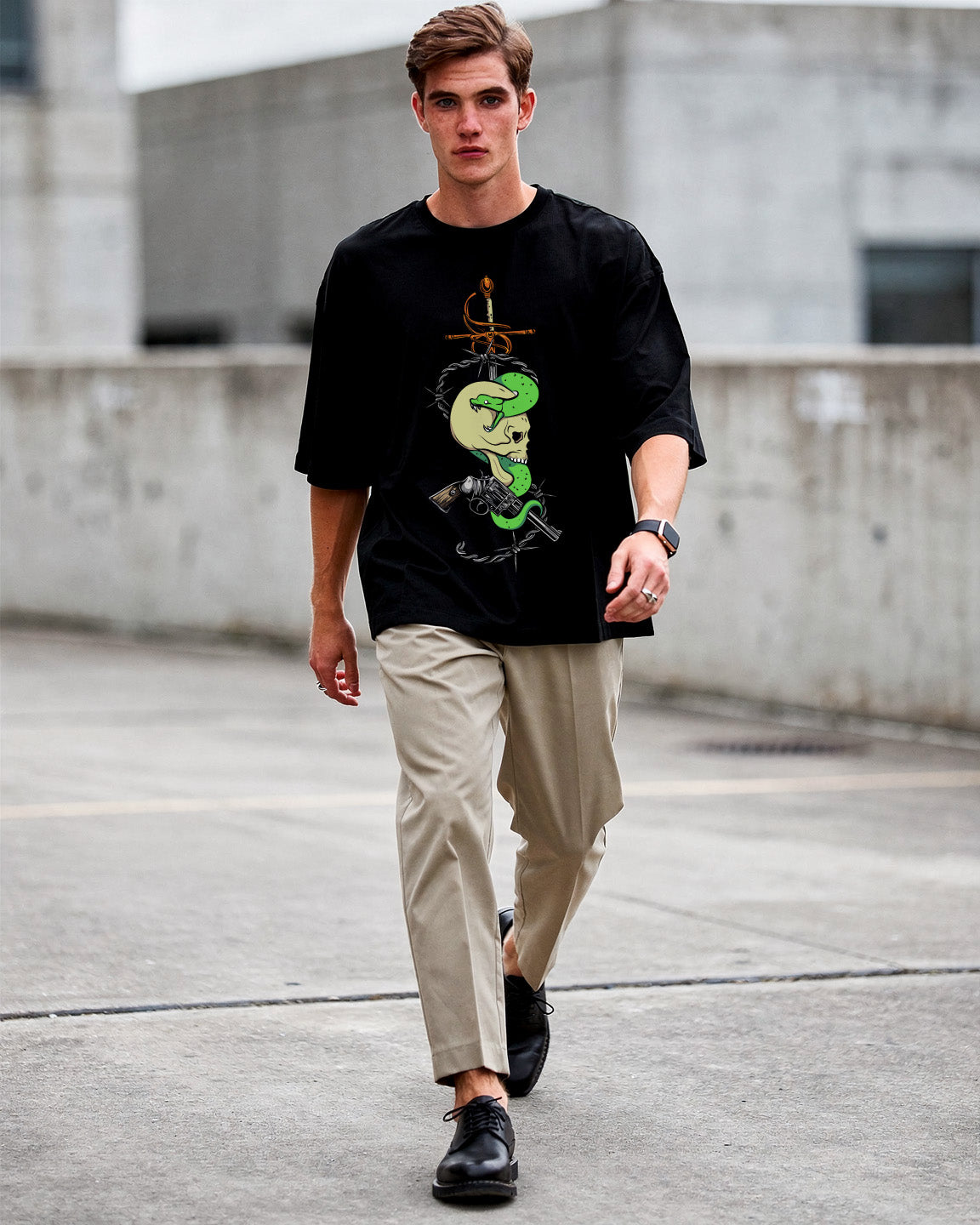 Man wearing a black t-shirt with a graphic design, beige pants, and black shoes on a concrete surface.