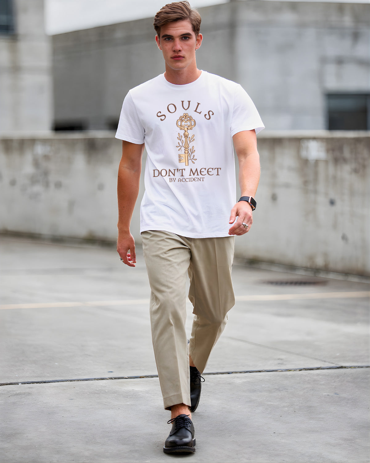 Man wearing a white t-shirt with text and graphics, beige pants, and black shoes on a concrete surface.