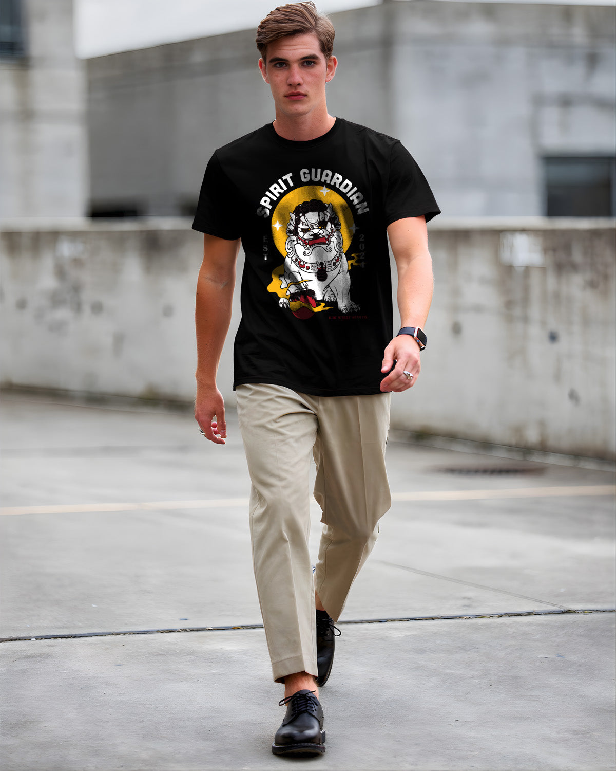 Man wearing a black t-shirt with a graphic design, beige pants, and black shoes in an urban setting.